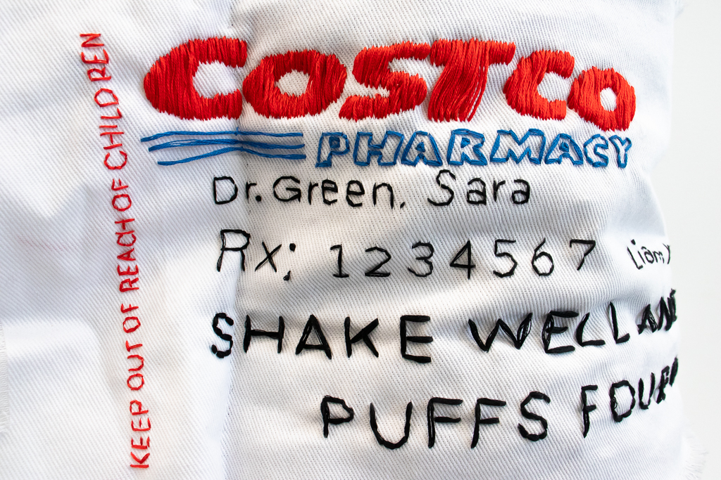 Close up detail image of inhaler sculptures tag, showing embroidery letters