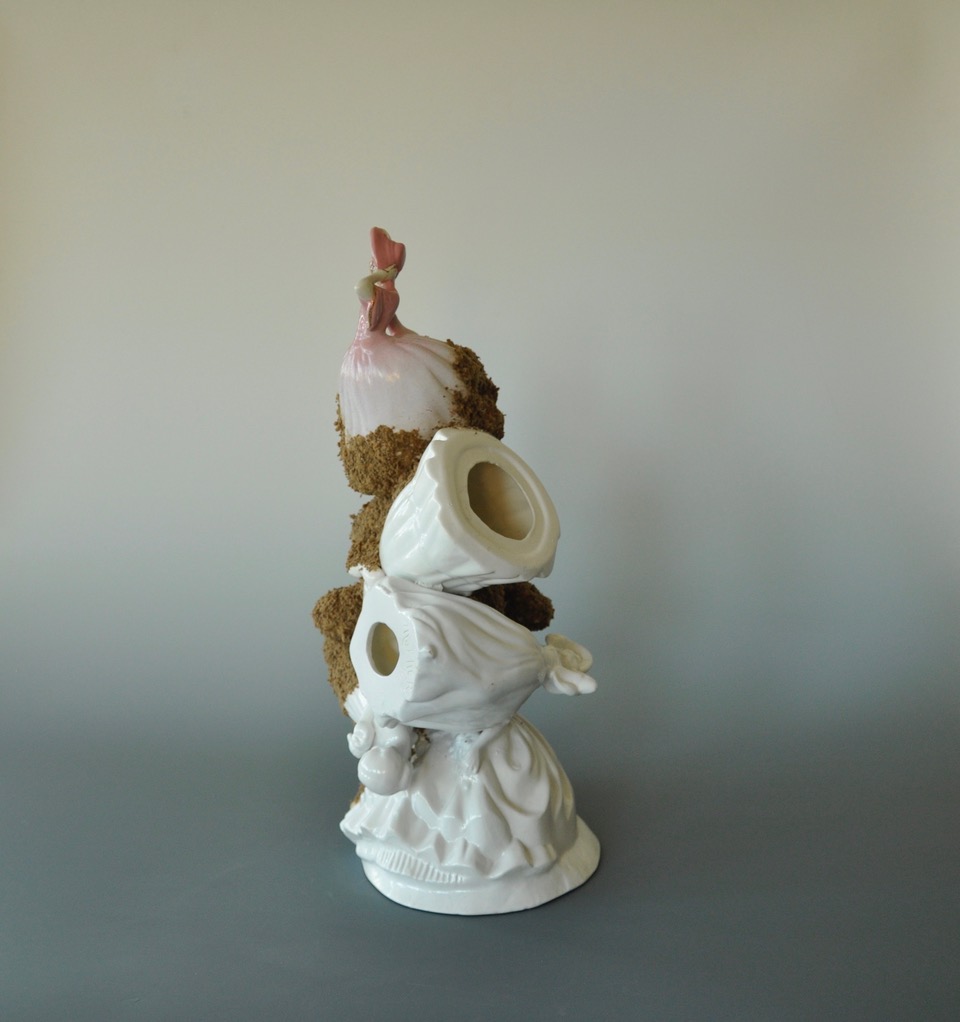 A sculpture consisting of 7 found porcelain female figurines in long dresses assembled in a column and partially bleached of colour. Gypsy moth eggs cover the northwest side of the column.
