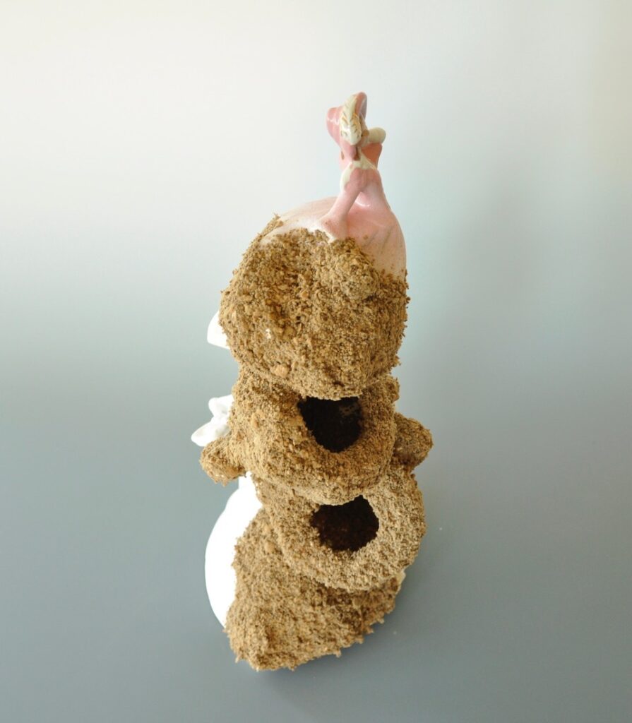 A sculpture consisting of 7 found porcelain female figurines in long dresses assembled in a column and partially bleached of colour. Gypsy moth eggs cover the northwest side of the column.