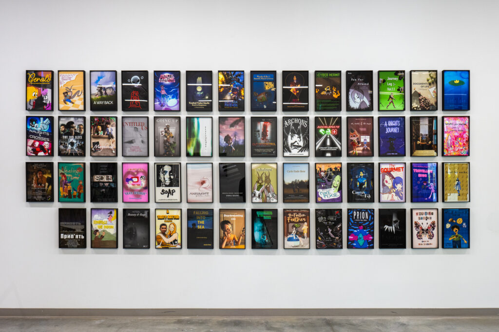 
A wall mounted display of dynamic media film posters in black frames with plastic coverings is organized in 14 columns and four rows.