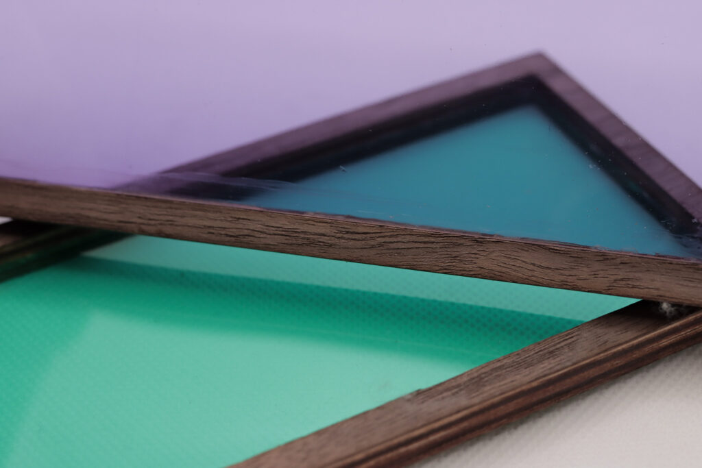 Wooden frame with a teal insert laying underneath a wooden frame with a purple insert 