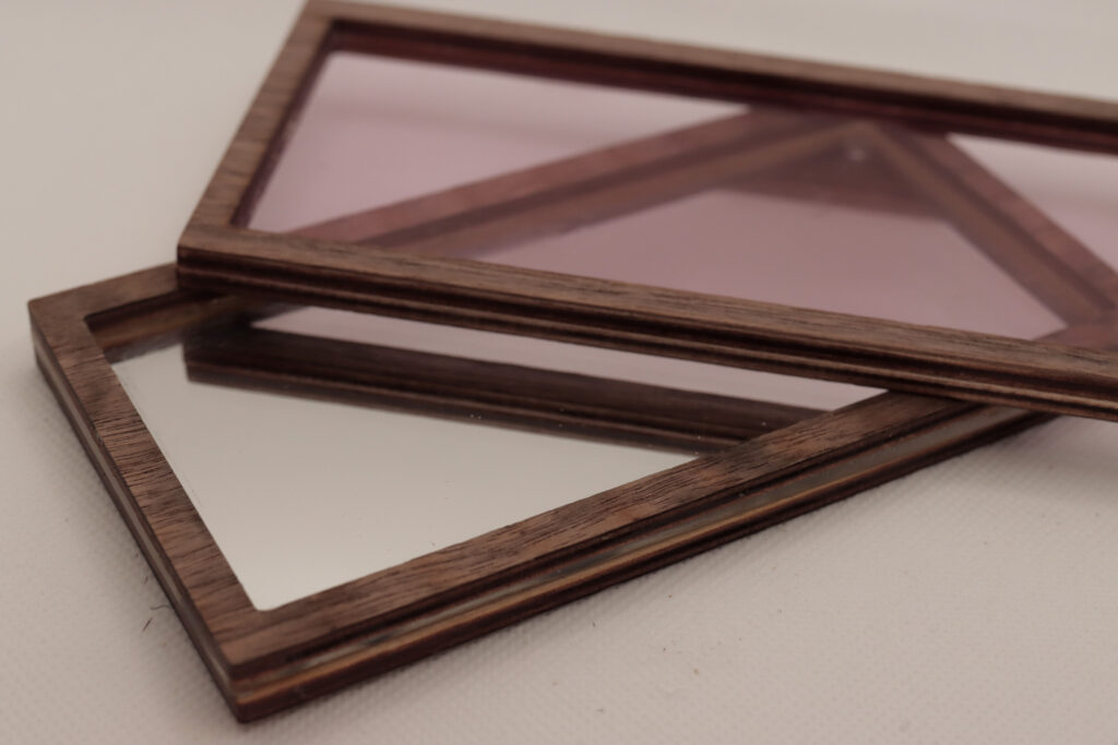 Wooden frame with a light pink insert laying on top of another wooden frame with a mirrored insert 