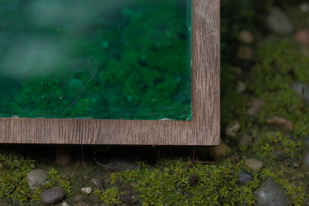 Close up of the corner of a wooden frame with a green insert sitting on a rocky, moss covered surface