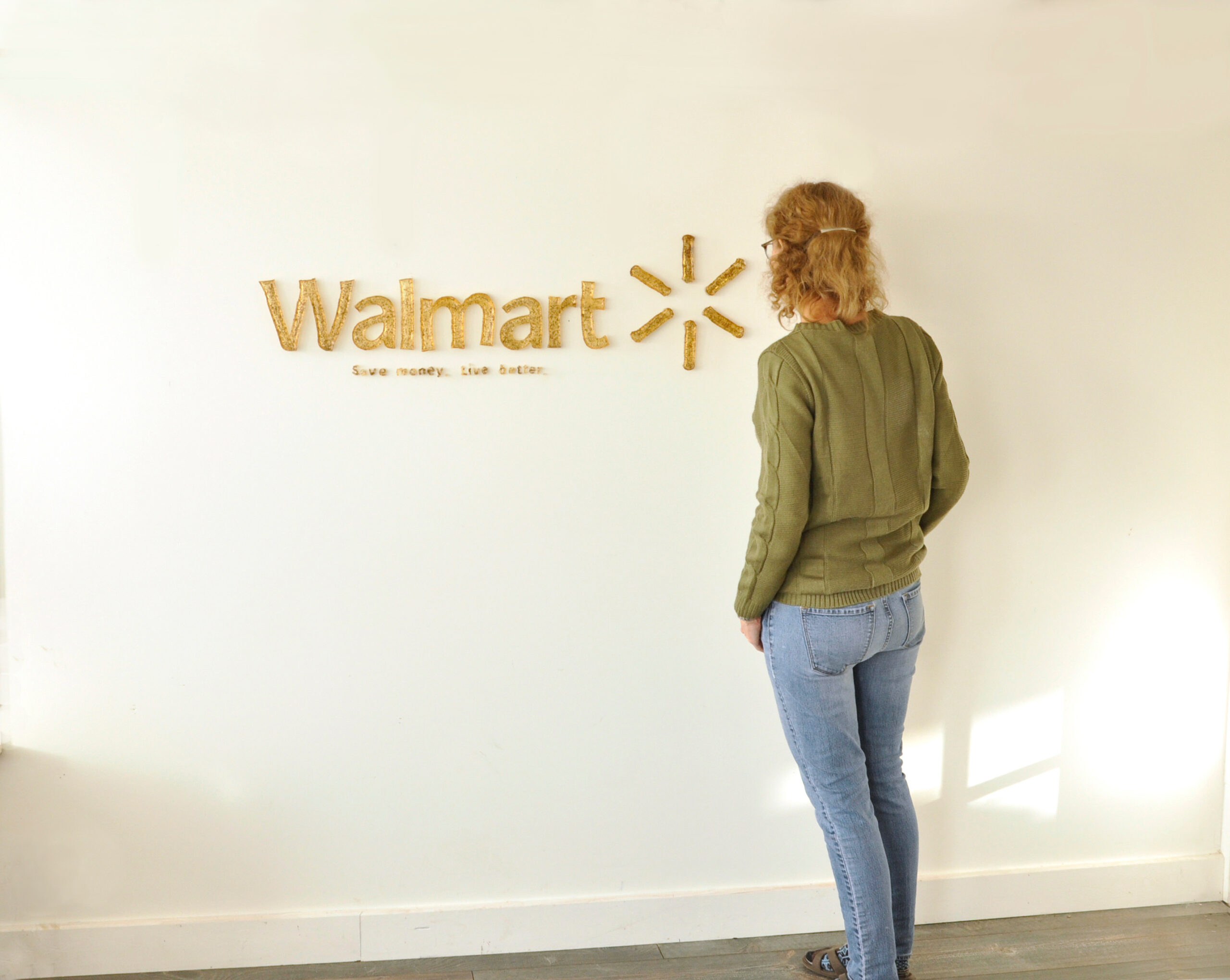artist standing beside sculpture mounted on a wall, the Walmart logo with slogan Save money. Live Better